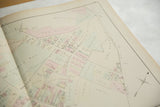 Angled view of an antique Woburn atlas page showing landowners and pastel-colored property plots.