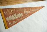Graphic of a conductor and crowd beneath a flame on a terra-cotta felt pennant.