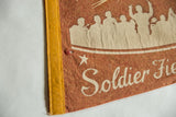 Detail of the yellow stitched binding and a pinhole on the aged terra-cotta felt pennant.