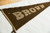 Close-up of vintage Brown University felt pennant, showing worn brown wool with tan letters and frayed top edge.
