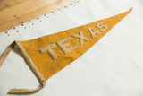 Mustard yellow felt pennant showing beige appliqued 'TEXAS' letters with visible wool texture.