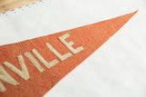 Close view of stitched block letters on the textured, aged orange wool of a felt pennant.