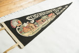 Angled view of a vintage Schoenbrunn Village pennant, showing felt texture and illustrated cabins.