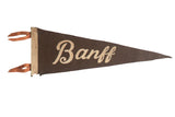 Vintage Banff felt pennant with dark brown ground, cream script lettering, and orange ties, 7x21 inches.