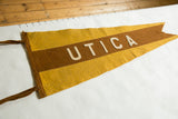 Aged felt pennant featuring 'UTICA' in cream letters on brown and mustard yellow stripes.