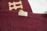 Fisch & Co. label on antique maroon felt pennant, revealing white stitching and aged texture.