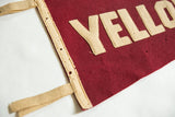 Corner of antique red felt pennant with beige 'YELLO' letters and perforated tie edge.