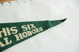 Pointed green felt pennant end with cream 'SIX HOBOES' lettering and visible texture.