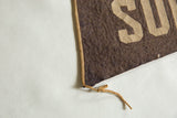 Braided tan trim and knotted tie on the corner of the antique brown felt pennant.
