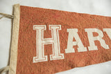 Vintage Harvard felt pennant showing white 'HAR' block letters and beige binding.