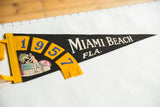 Vintage Miami Beach Fla. pennant showing 1957, woman on beach graphic, and white text.