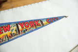 Blue felt New York City pennant with red text and RCA Building illustration.