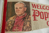 Vintage pennant detail showing red 'WELCOME Pope' text on ivory felt with creases.