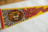 Bold lion graphic, zebra stripes, and red text on yellow felt pennant.