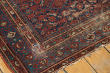 Vintage Malayer rug: intricate brick red and blue borders, visible wear, and a corner stain.