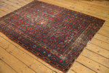 Corner of vintage Malayer rug showcasing intricate brick red, blue boteh borders and time-softened pile.