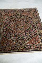 Angled view of a vintage Persian Sarouk rug with a navy field and red floral medallion.