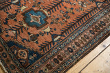 Close-up of vintage Kurdish Hamadan rug showing low pile texture, madder red field, and navy geometric border.