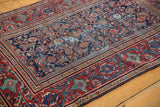 Corner of a vintage Persian Mahal rug, navy Herati motif, cherry red Serbend border, visible foundation wear.