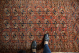 Dusty brick red antique Tekke rug with repeating navy, ivory, bronze gul motifs, low pile wear.