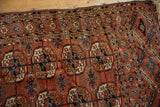 Antique Tekke rug with repeating gul motifs in dusty brick red, navy, and ivory, revealing low pile.