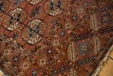 Antique Tekke rug: repeating gul motifs, low pile in dusty brick red, ivory, navy blue.