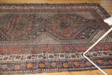 Antique Qashqai rug corner, madder red, navy, ivory geometric border, and lightly tattered fringe.