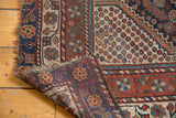 Hand-knotted Qashqai rug corner revealing worn madder red and navy pile, light fringe tatter, and foundation.