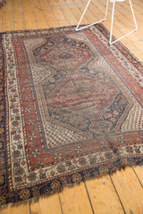 Antique Qashqai rug corner showing madder red borders, geometric motifs, light tatter, and evident foundation.