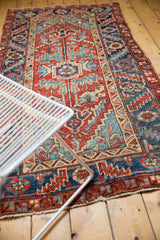 Geometric Heriz rug detail in deep cherry red, dusty teal, with low pile and knot heads.