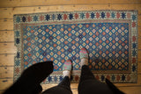 Corner of antique Kuba rug runner with geometric border, blue field, and tattered edge.