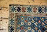 Antique Kuba rug corner, featuring geometric star border, blue field, and tattered edge.