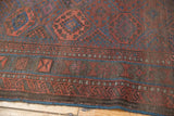 Close-up of antique Belouch rug's geometric patterns in madder red and deep indigo blue.