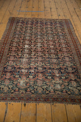 Antique Malayer rug's fine boteh pattern with charcoal field, showing worn fringe and overcast end.
