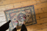 Antique Persian Kerman mat with a floral medallion, shown for scale on a hardwood floor.