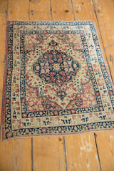 Full view of an antique Persian Kerman rug with a navy floral medallion on an ivory field.