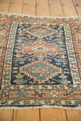 Angled detail of geometric motifs in navy, terracotta, and teal with worn fringe.
