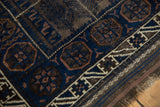 Antique Belouch bag face rug close-up: indigo, charcoal geometric patterns, fringed end.