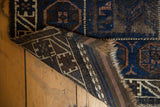 Belouch rug corner showing deep indigo geometric patterns, hand-knotted back, and tattered end.