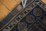Antique Persian Belouch rug corner detail with deep indigo, charcoal brown geometric border, and aged fringe.