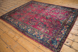 Vintage Lilihan rug corner showing raspberry field, navy blue floral border, and exposed foundation.