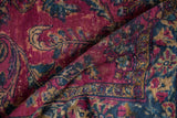 Folded vintage Lilihan rug displaying raspberry red field, navy blue vinery, and floral motifs.