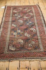 Bottom corner of vintage Belouch runner with madder red border, geometric gul motifs, and fringe.