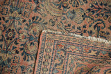 Dusty blush field with blue floral vinery, patterned border, and tattered fringe.