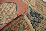 Folded vintage Tabriz rug detail showing dusty rose field, navy floral botehs, and fringed end.
