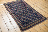 Antique Belouch rug's repeating germinating flower motif, navy field, madder border, and worn pile.