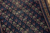 Detail of antique Belouch rug featuring navy, red, and ivory germinating flower pattern and low pile.