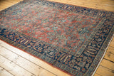 Intricate indigo border and brick red field with splayed floral vinery and visible wear.