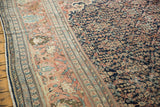 Terra cotta border with palmettes, navy floral field, low pile, time-softened tones.