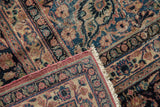 Folded corner of vintage Meshed carpet, showing its fringe, blush border, and worn floral patterns.